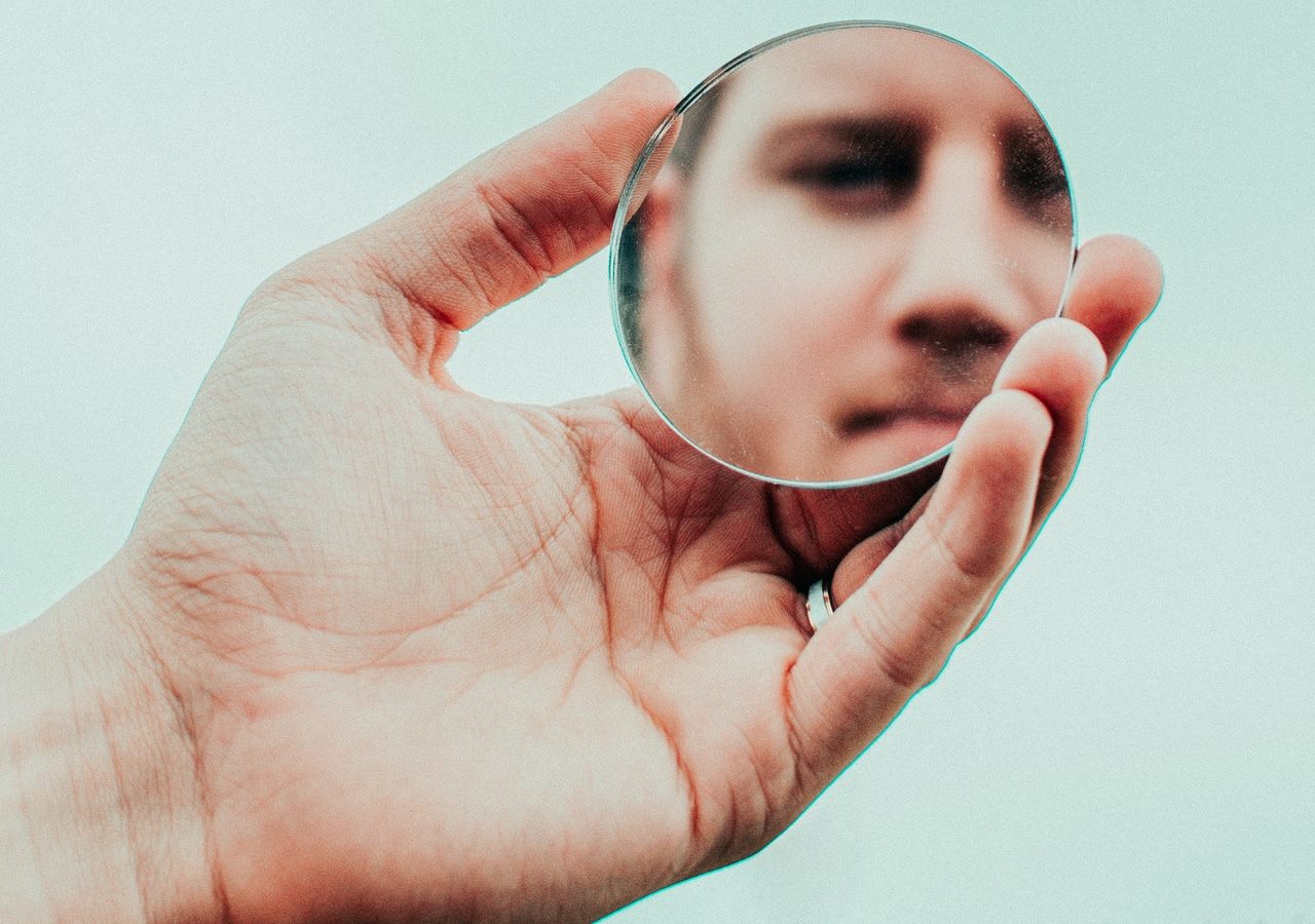 A man holding a small round mirror looking at himself