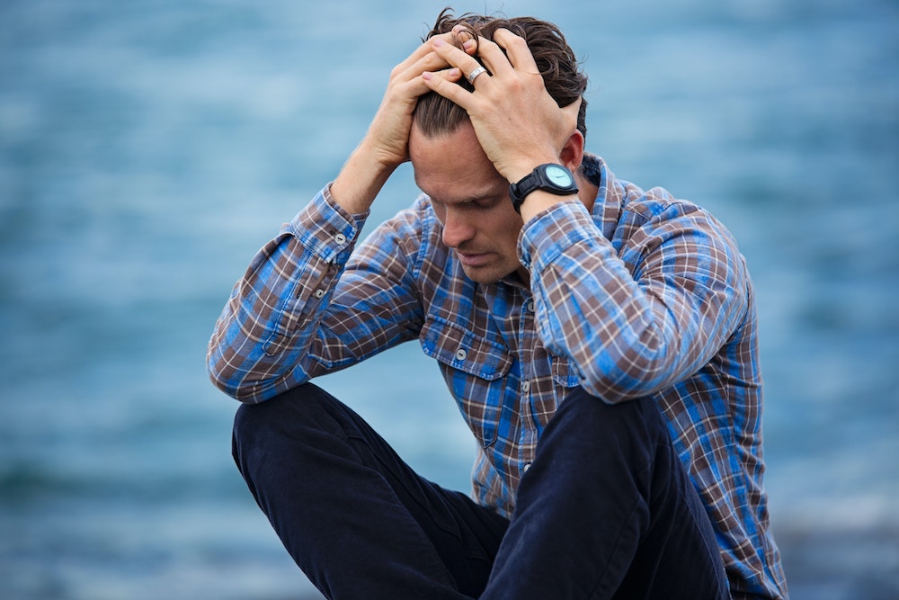 Man in Blue and Brown Plaid Dress Shirt Touching His Hair and looking anxious