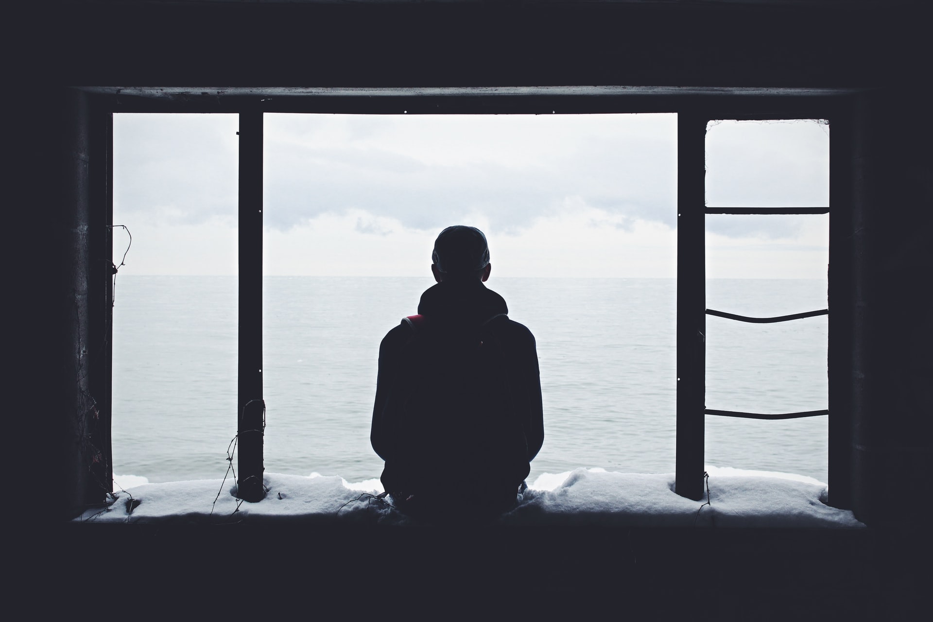A man sitting on a window sill overlooking the ocean
