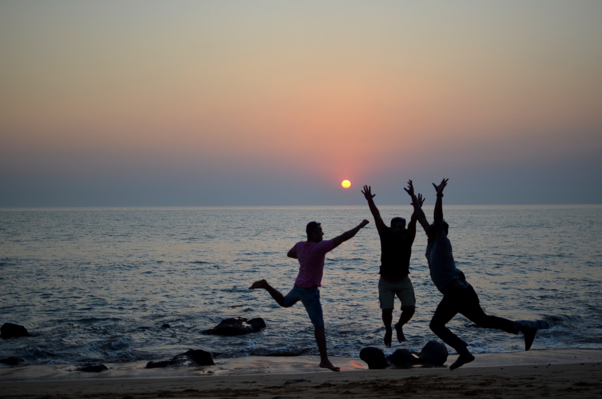 Silhouette of 3 happy persons enjoying the sunset on the beach