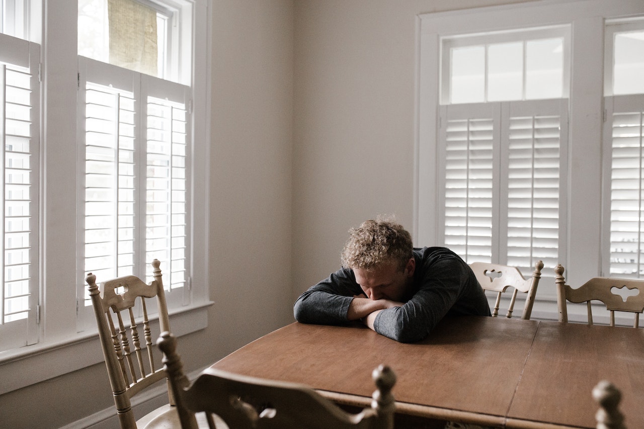 A sad man resting on his arms on the dining table