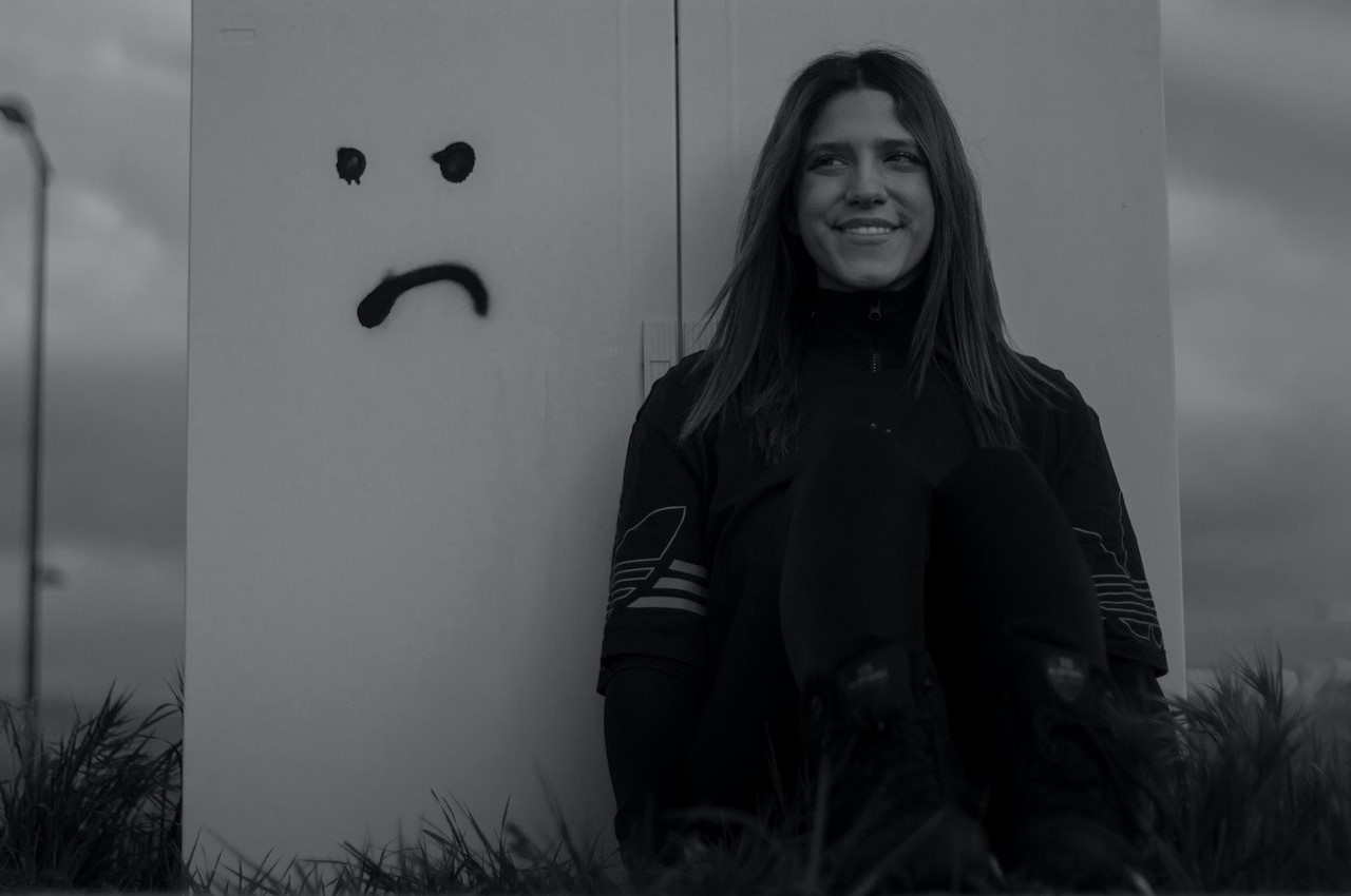 A woman smiling next to a painted sad face on the wall