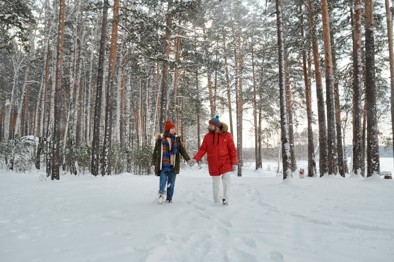 A couple happily walking in the snow, with tall trees behind them