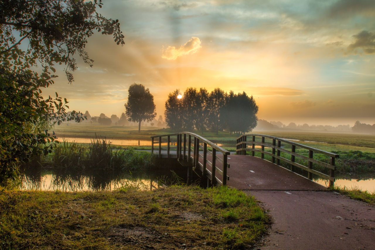 Idyllic sunrise scene with misty bridge, river, and tranquil landscape.