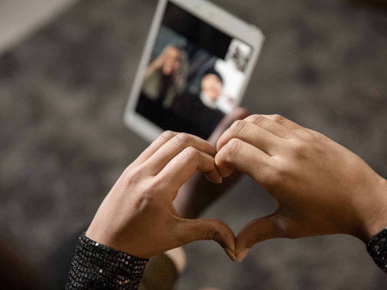 Close-up of hands forming a heart shape during a video call on a tablet